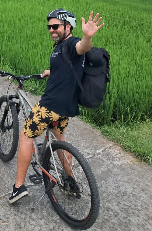 Smiling guest waving with his bike on a rice field path